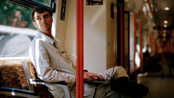DJ Fred Again sitzt in einer Straßenbahn, mit Kopfhörern und Laptop ausgestattet und starrt nach draußen.